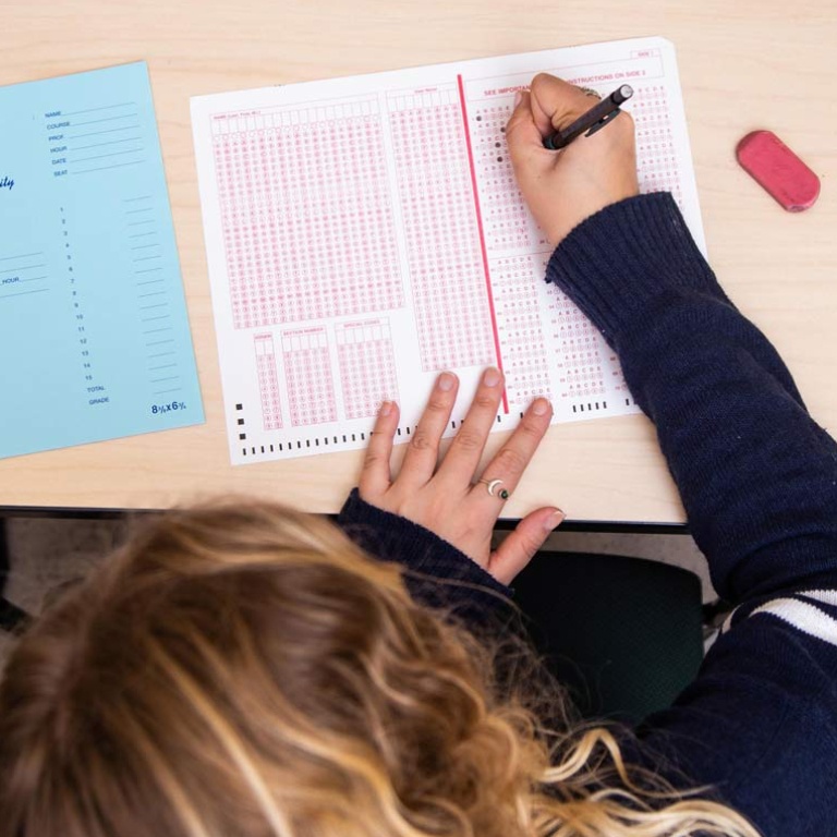 Overhead image of a person working on a scantron test on a desk.