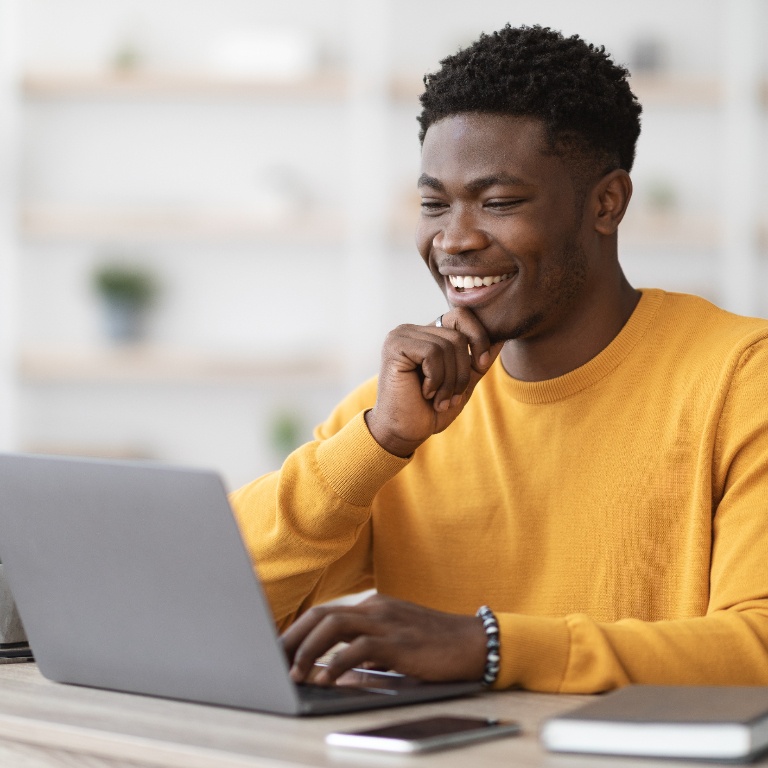 Man sitting at a desk and smiling while working on a laptop.