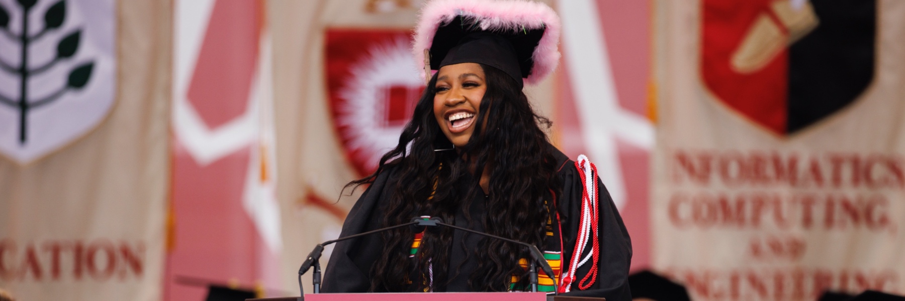 A young black woman in academic regalia smiles while delivering a commencement speech at IU