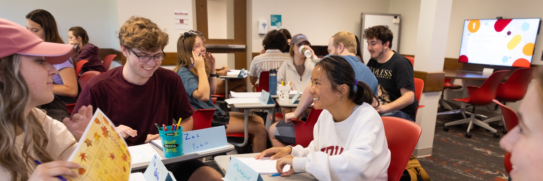 A group of students conversing at desks in a classroom.