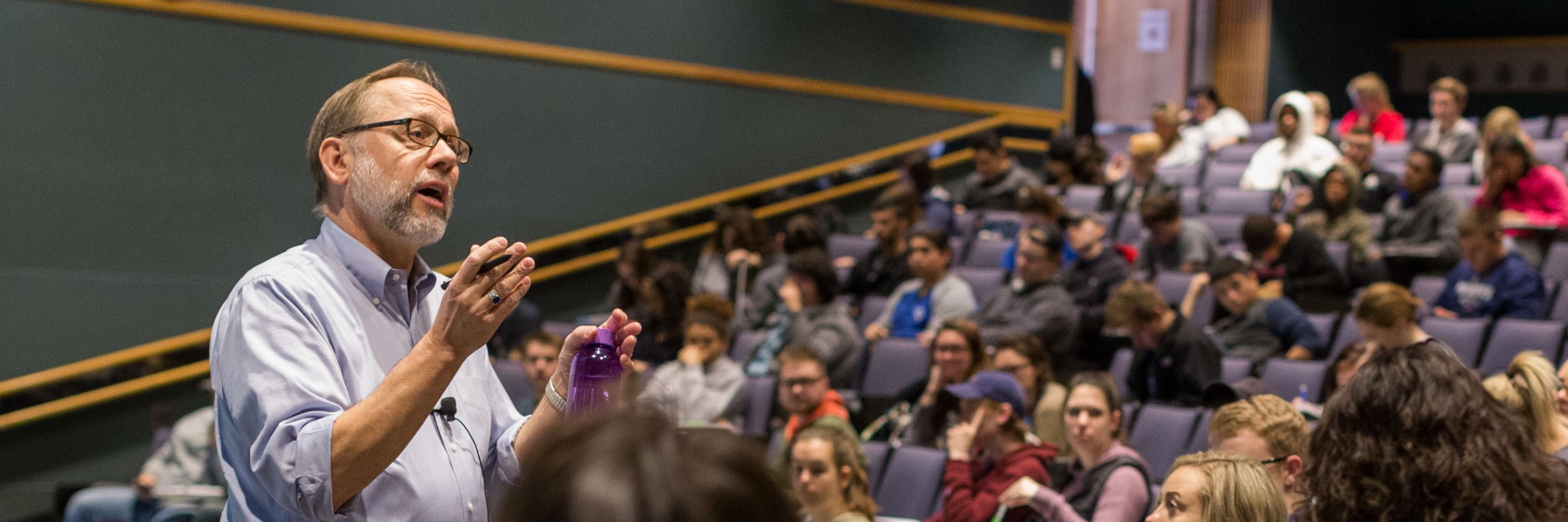 A chemistry professor animatedly addresses a large lecture hall of students