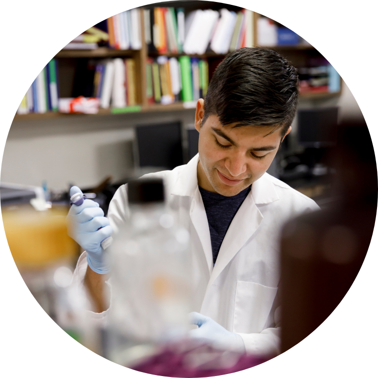 Student wearing a labcoat and smiling while working.