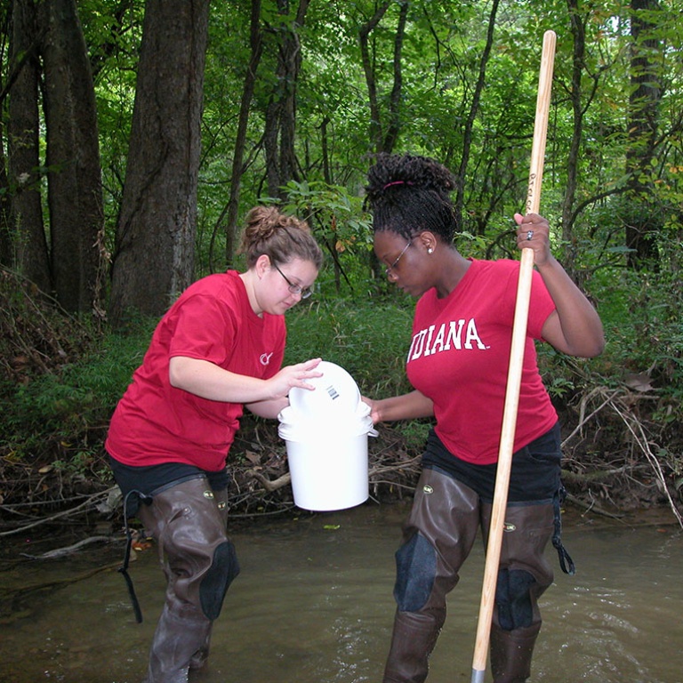 Two students wearing Indiana apparel while working in a creek bed.