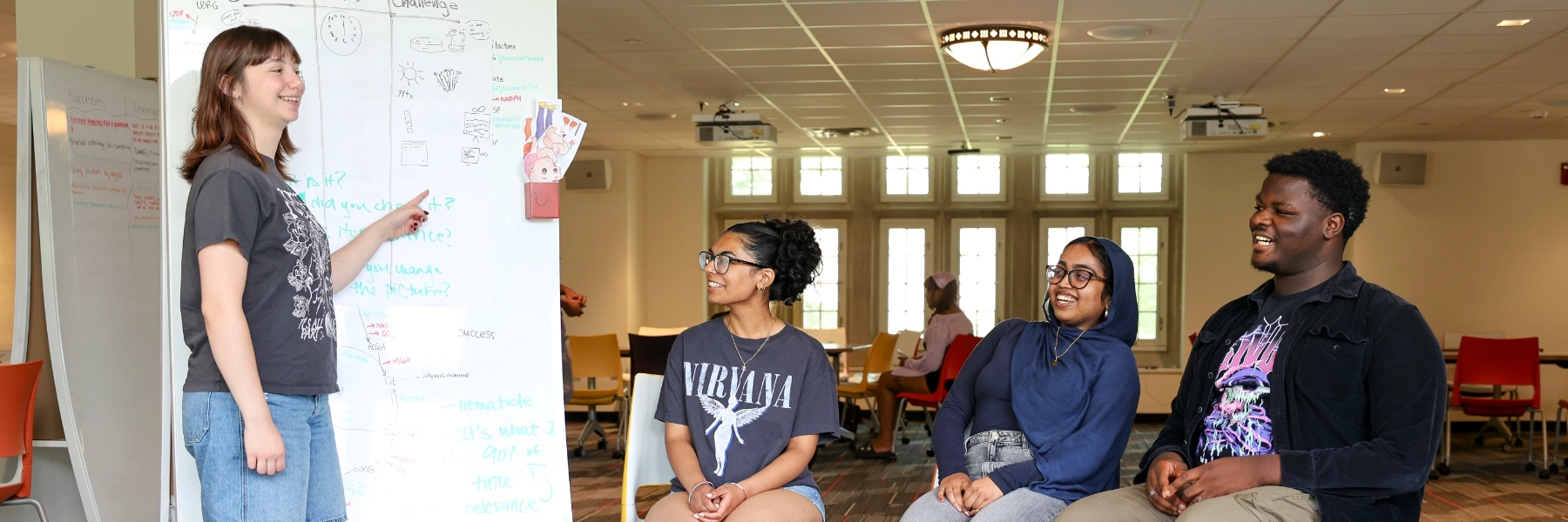 A student smiles while informally presenting their research to other students