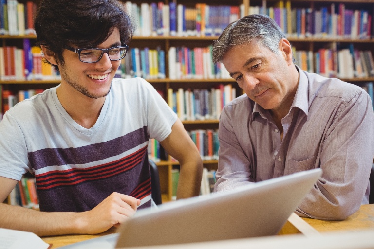 A student and professor sitting and working together at a desk in a library.