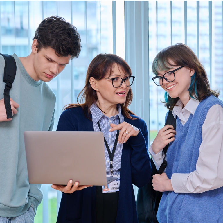 Two students and an instructor standing around a laptop and talking.